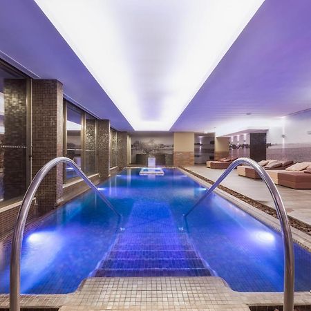 Lago Montargil&Villas Esterno foto The photo shows a modern indoor swimming pool area. The pool features a sleek design with steps leading into the water and a gentle curve at the sides. The water is illuminated in a blue hue, enhancing the relaxing atmosphere. Surrounding the pool ar