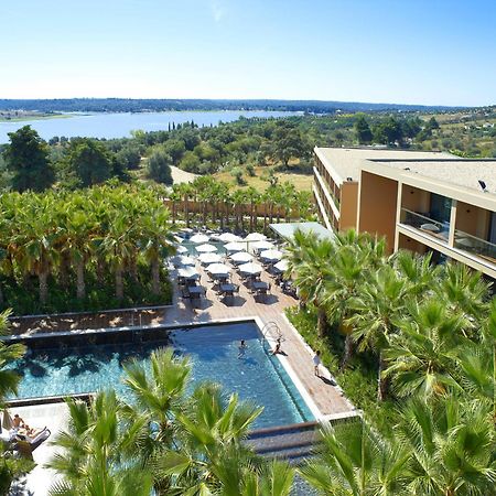 Lago Montargil&Villas Esterno foto The photo shows a scenic view of a modern hotel or resort. In the foreground, there is a swimming pool surrounded by palm trees, with lounge chairs positioned beside it. Sun umbrellas provide shade over the chairs. The background features a lush land