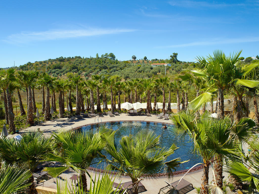 Lago Montargil&Villas Esterno foto The photo depicts a beautiful outdoor area featuring a circular swimming pool surrounded by palm trees. The pool area has several lounge chairs arranged around it. In the background, there is a lush green hillside, and the sky is clear with a bright 