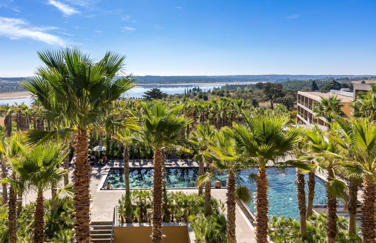 Lago Montargil&Villas Esterno foto The photo depicts a picturesque resort landscape with a clear blue sky. In the foreground, there are tall palm trees surrounding a swimming pool area. The swimming pool has a modern design and is surrounded by lush greenery. In the background, you ca