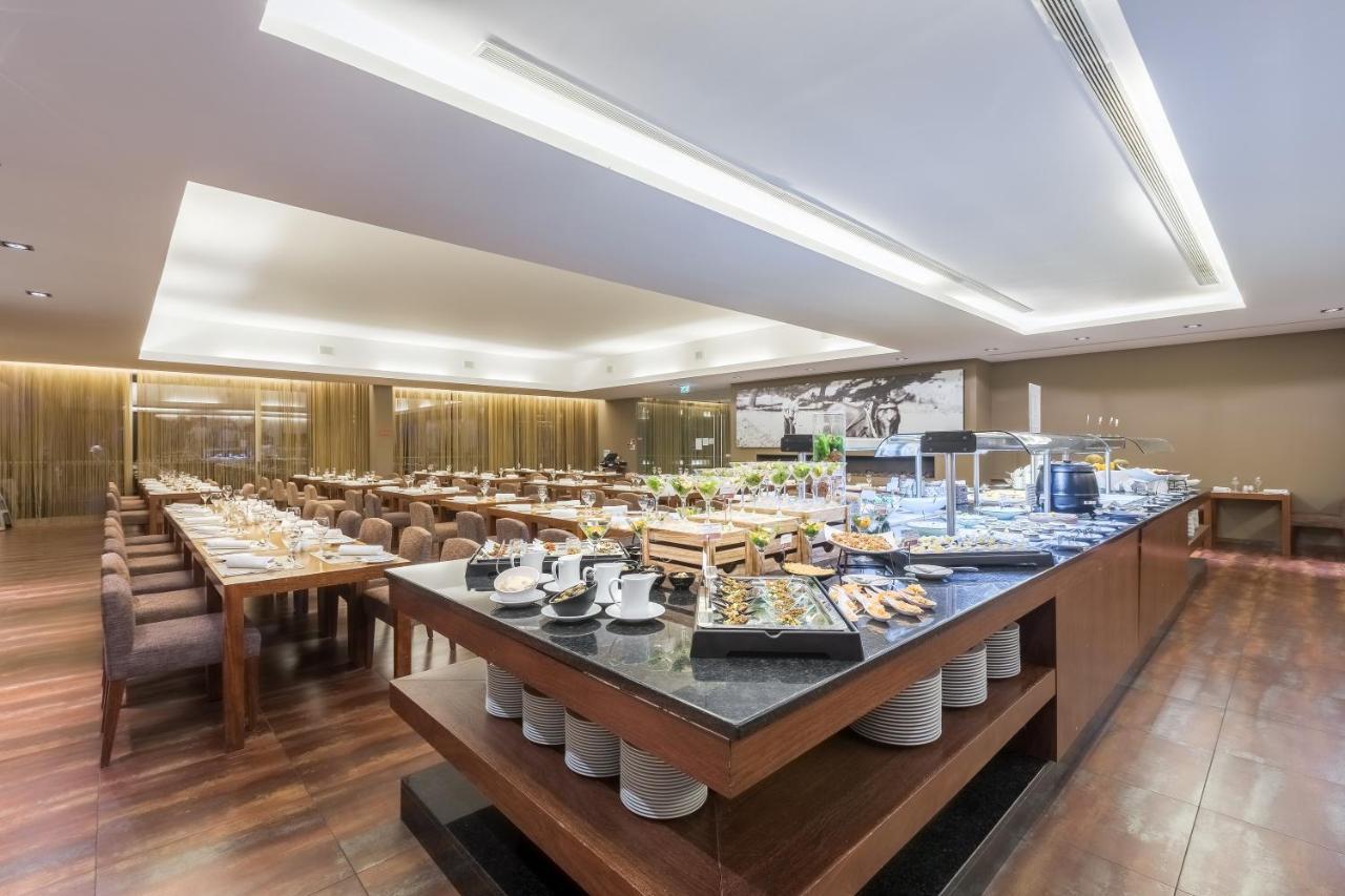 Lago Montargil&Villas Esterno foto The photo displays a spacious restaurant interior, featuring a well-organized dining area with multiple tables set for patrons. In the center, there is a large buffet station filled with an array of food items. The decor is modern and elegant, with w