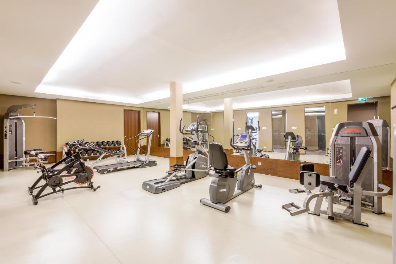 Lago Montargil&Villas Esterno foto The image shows a modern gym interior featuring various exercise equipment. On the left, there are free weights and weight benches. In the center, there are multiple machines, including a stationary bike and an elliptical. The space is well-lit with 