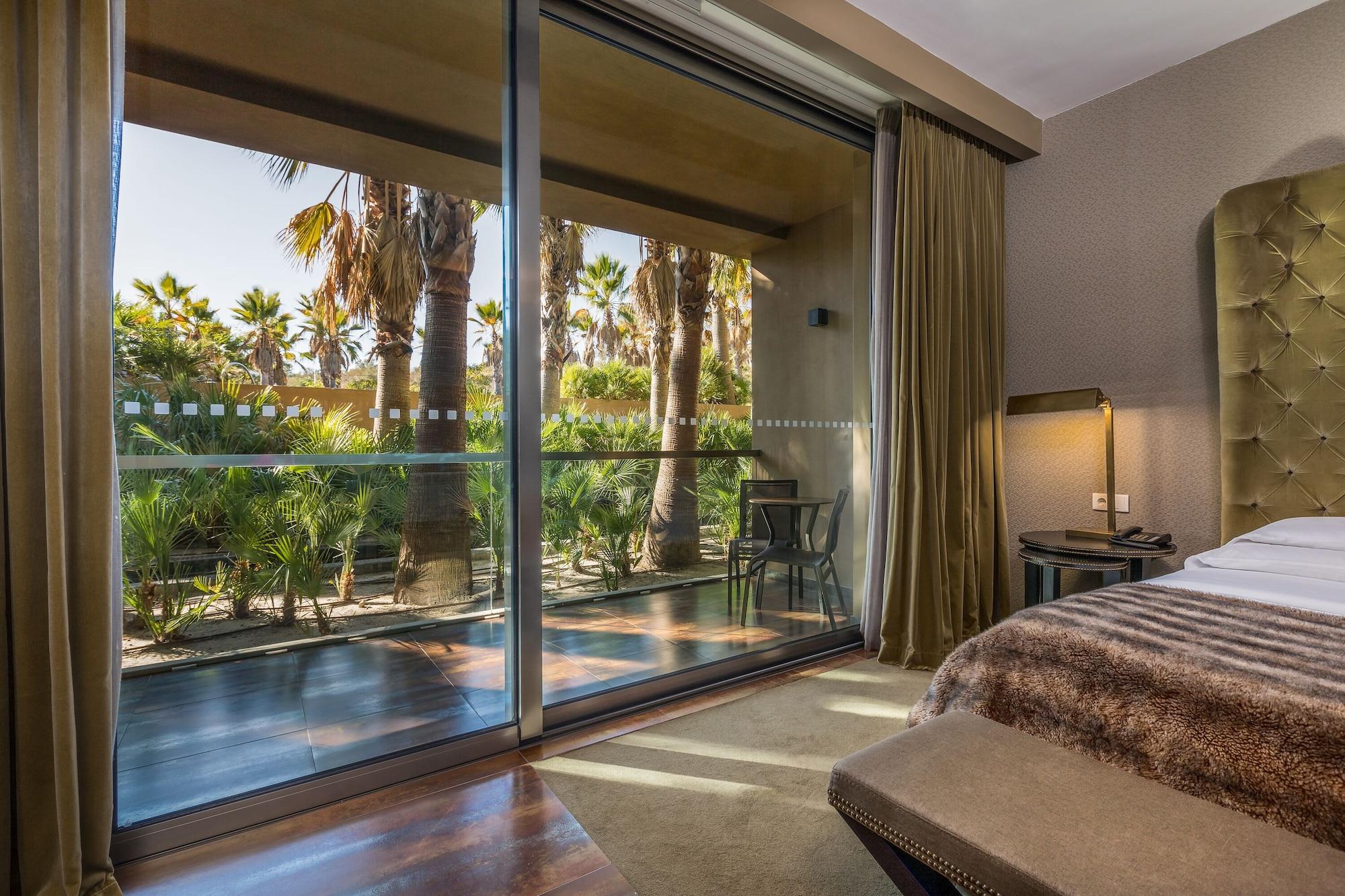 Lago Montargil&Villas Esterno foto The photo shows a bedroom with large glass doors that lead out to a balcony or terrace. The view outside features palm trees and lush greenery, indicating a tropical or warm climate. Inside the room, there is a bed, a bedside table with a lamp, and a