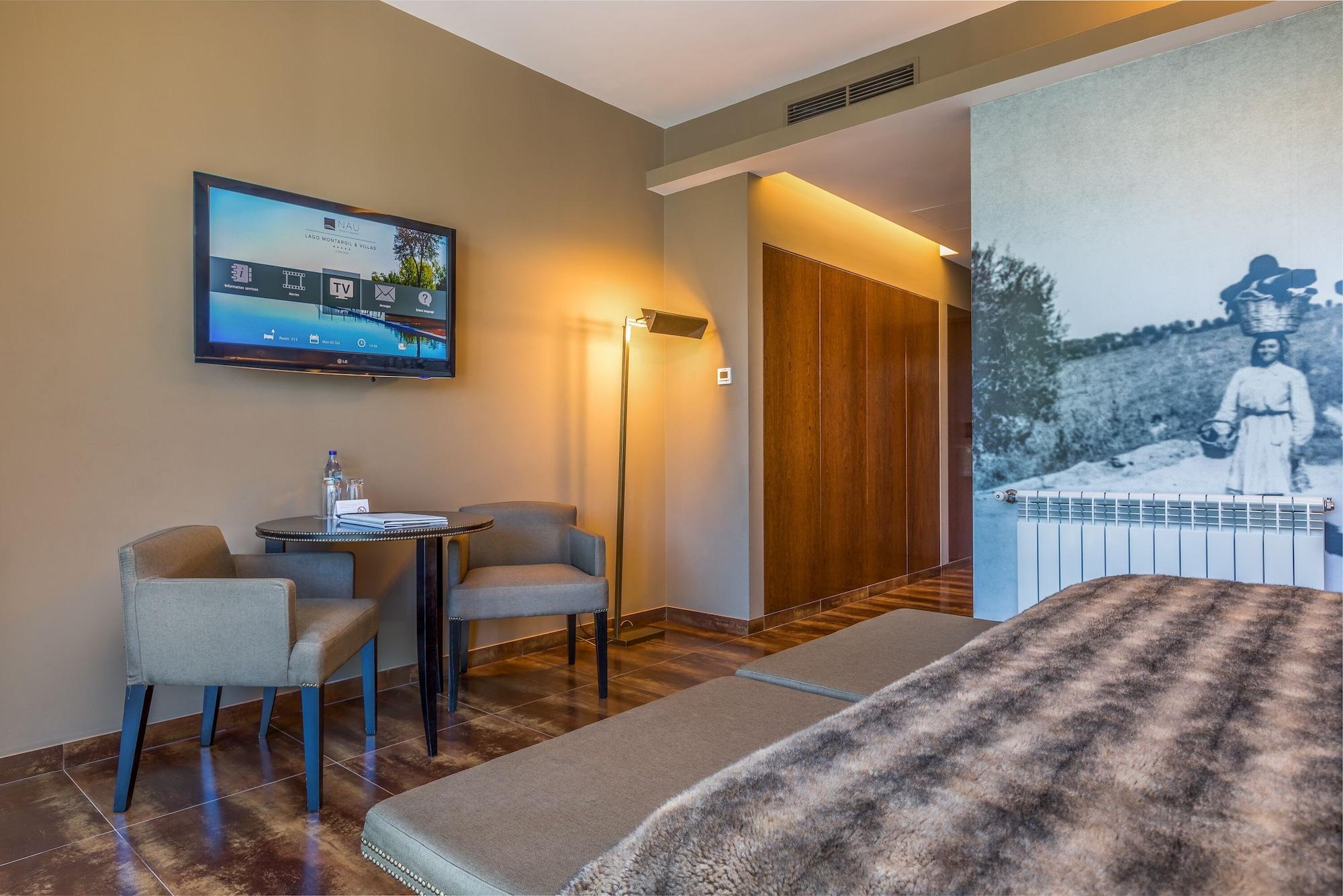 Lago Montargil&Villas Esterno foto The photo shows an interior of a room, likely a hotel or a modern living space. In the foreground, there is a bed with a textured brown blanket. To one side, there are two comfortable chairs and a small table, possibly with a bottle of water. A flat-
