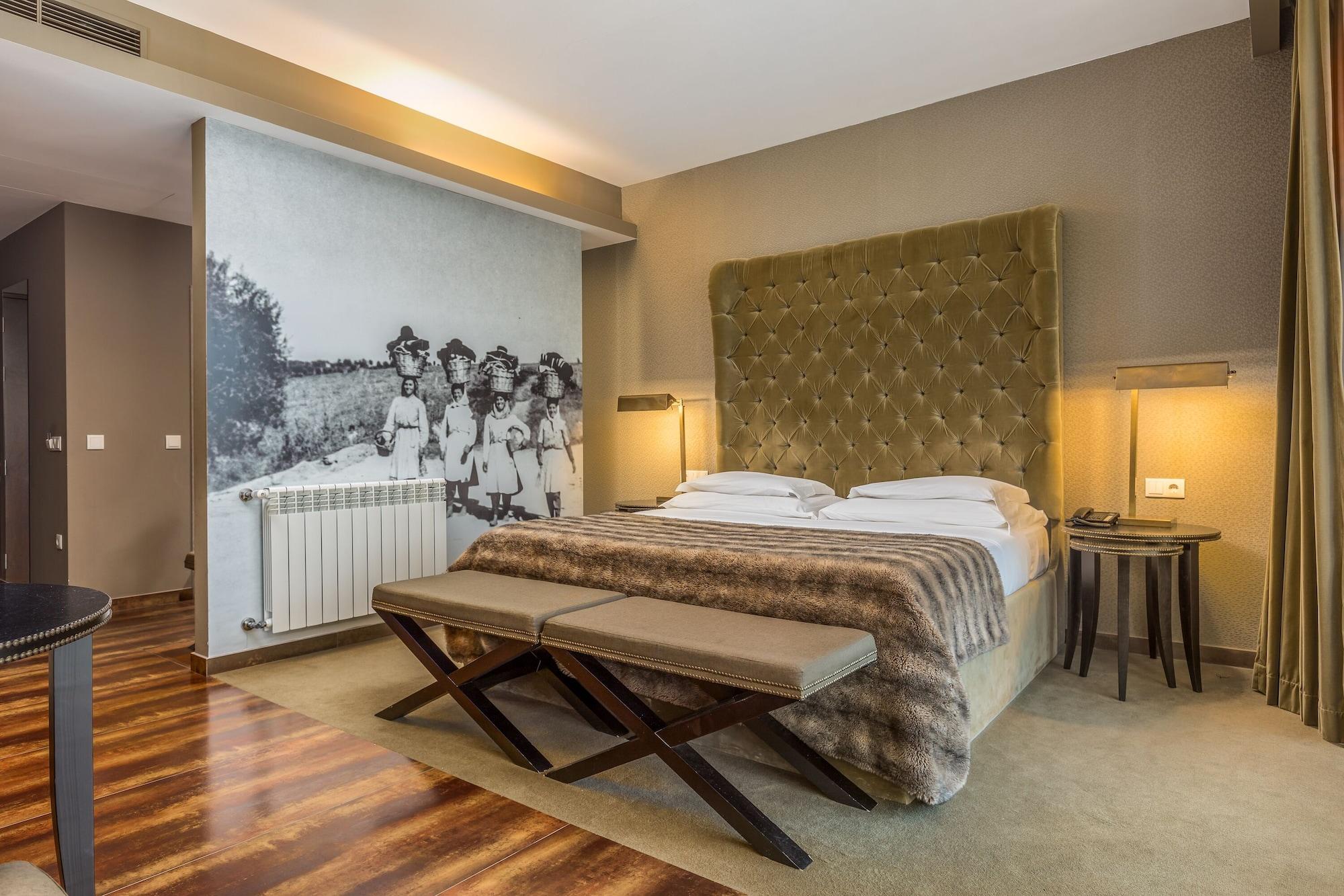 Lago Montargil&Villas Esterno foto The photo shows a modern hotel room with a large, plush bed that has a tufted, green headboard. The bedding is white with a textured blanket at the foot of the bed. A decorative wall behind the bed features a black and white mural of children in a fi