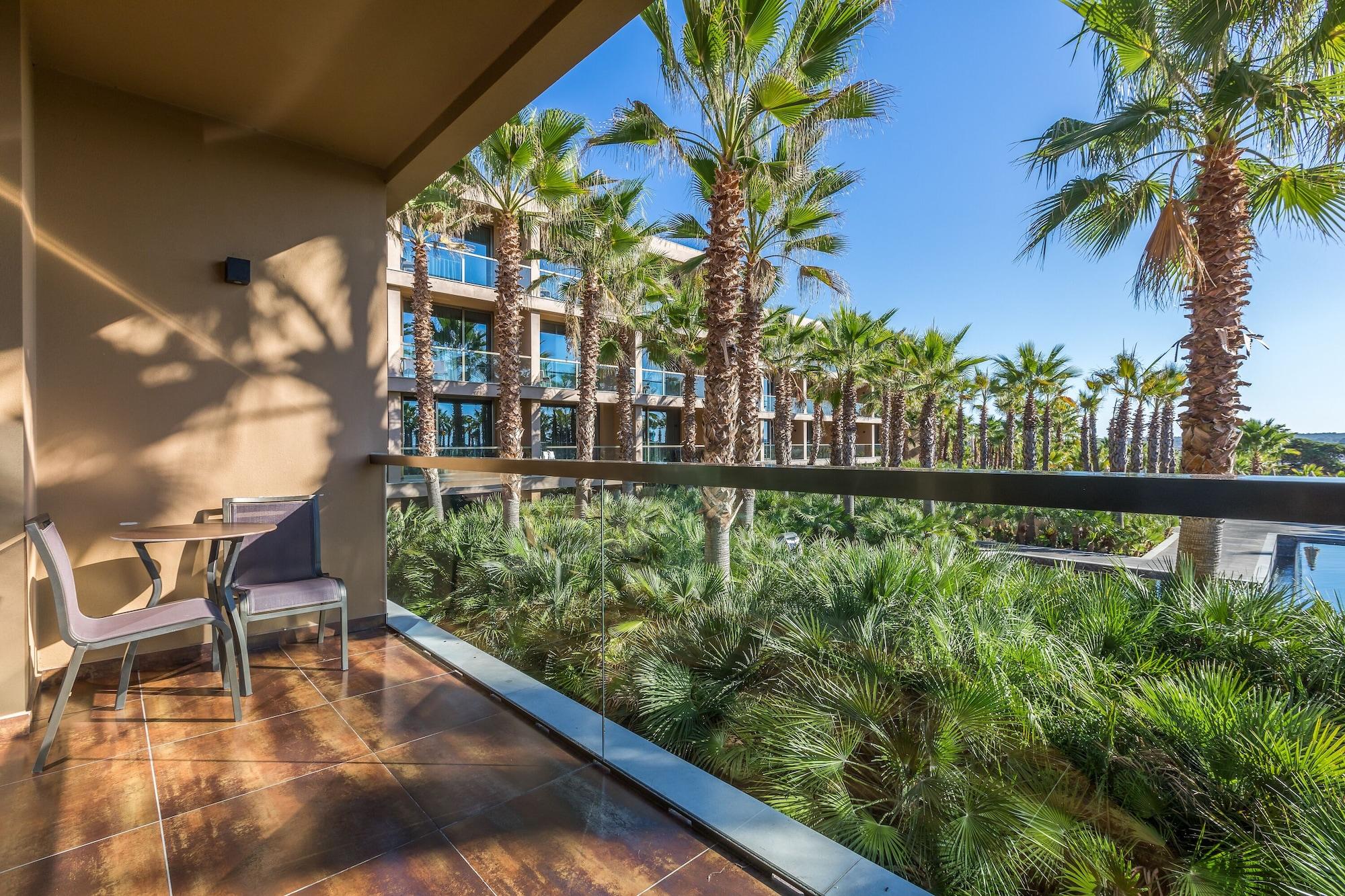 Lago Montargil&Villas Esterno foto The photo shows a balcony with modern furniture, including a chair and a small table. In the background, there are tall palm trees and lush greenery, suggesting a tropical or resort-like setting. The buildings in the distance are likely part of a hot