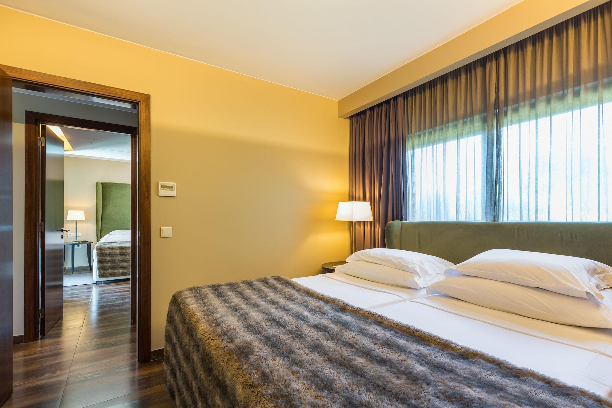 Lago Montargil&Villas Esterno foto The photo shows the interior of a well-furnished hotel room. It features two beds with white linens and a gray decorative throw on top. The walls are painted a warm yellow, and there are floor-to-ceiling windows covered with dark curtains that allow 