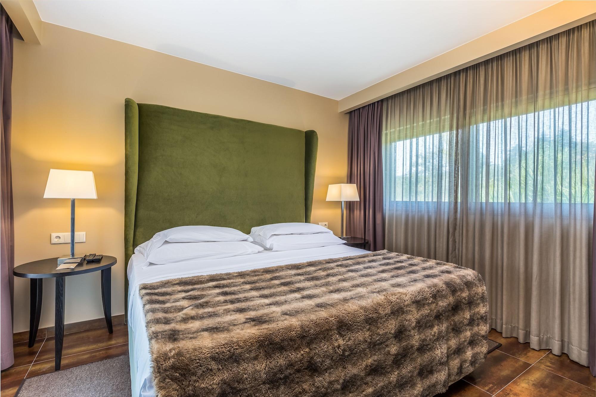 Lago Montargil&Villas Esterno foto The photo shows a cozy hotel room featuring a large bed with two white pillows and a fur-style blanket draped over it. Behind the bed is a tall, green headboard that adds a touch of color to the room. On either side of the bed are bedside tables, eac