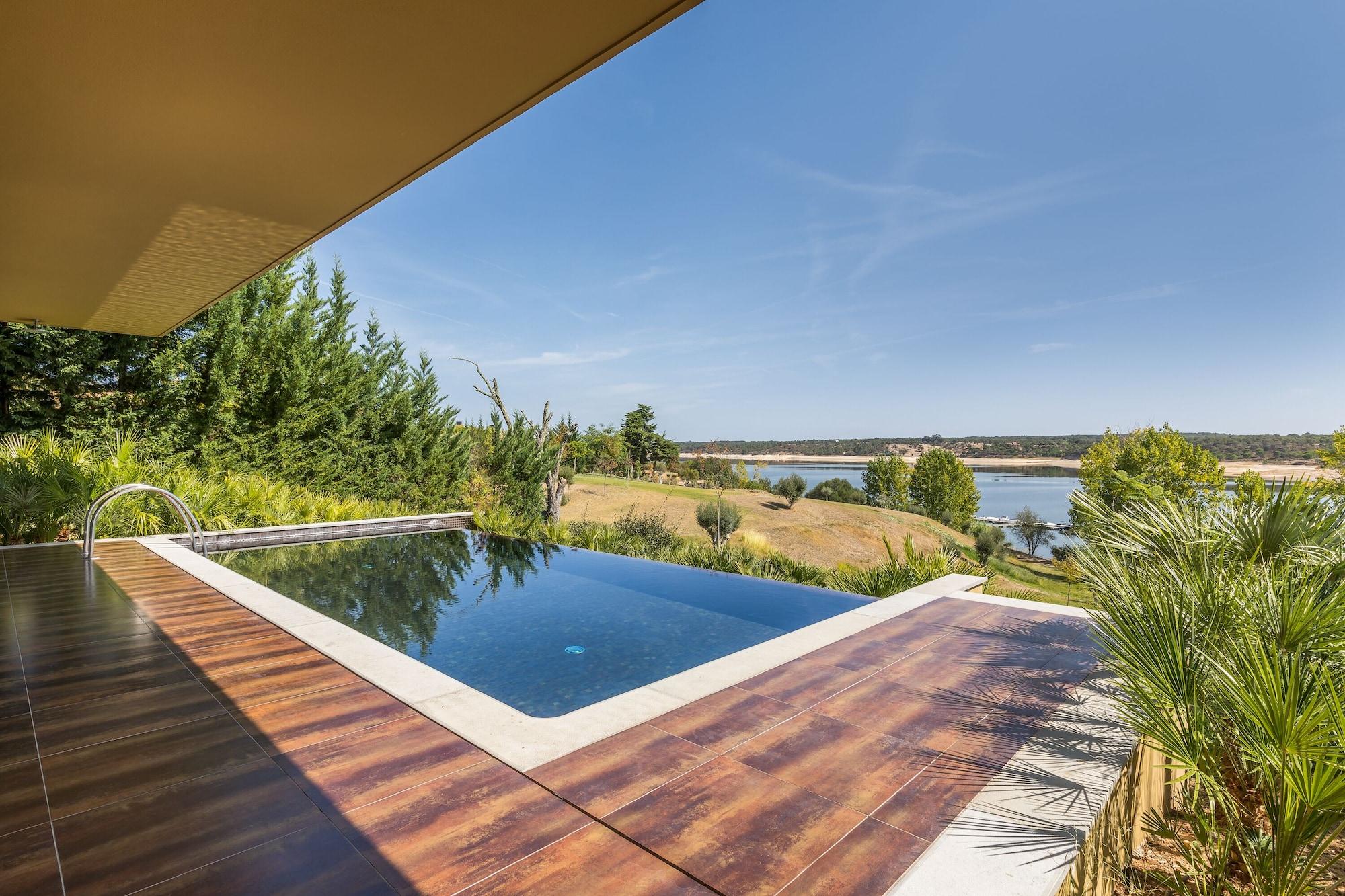 Lago Montargil&Villas Esterno foto The photo shows a luxurious infinity pool situated on a terrace or deck. The pool features a sleek, modern design with a dark blue surface that reflects the surrounding scenery. In the background, there is a landscape of rolling hills and a body of w