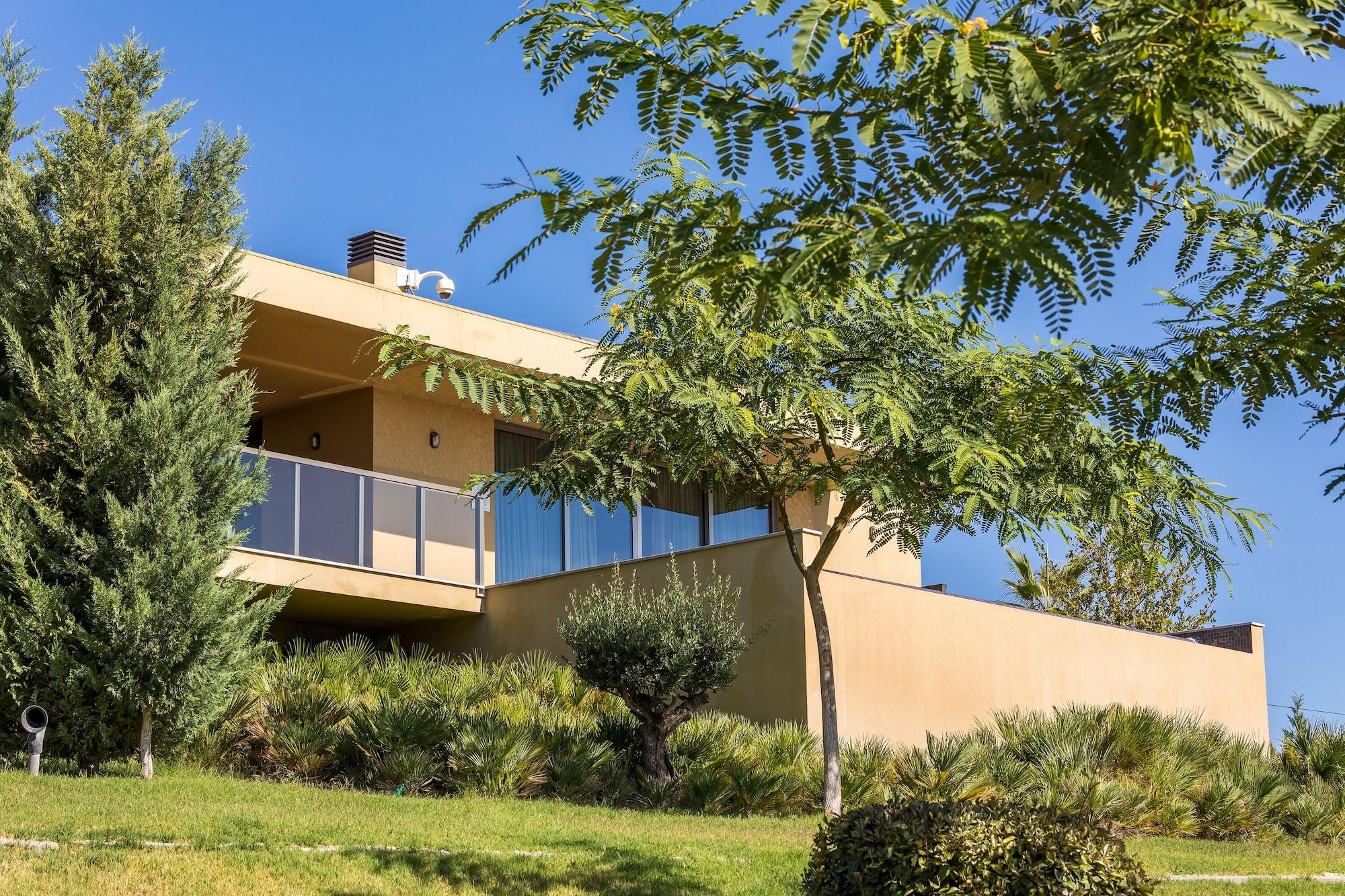 Lago Montargil&Villas Esterno foto The photo showcases a modern house situated on a grassy slope. The house features a light-colored exterior with large windows and a balcony. Surrounding the building are several trees and landscaping that enhances the natural environment. The sky is 