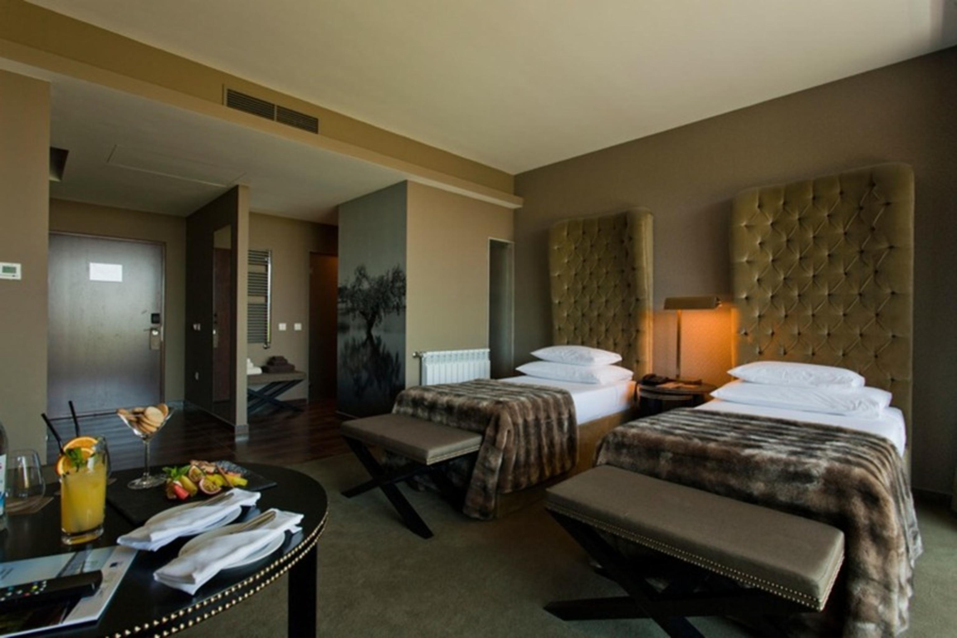 Lago Montargil&Villas Esterno foto The photo shows a stylish hotel room featuring two beds with plush, upholstered headboards. The room has a modern and elegant design, with earthy tones dominating the decor. A small round table is set up in the foreground, displaying a drink and some