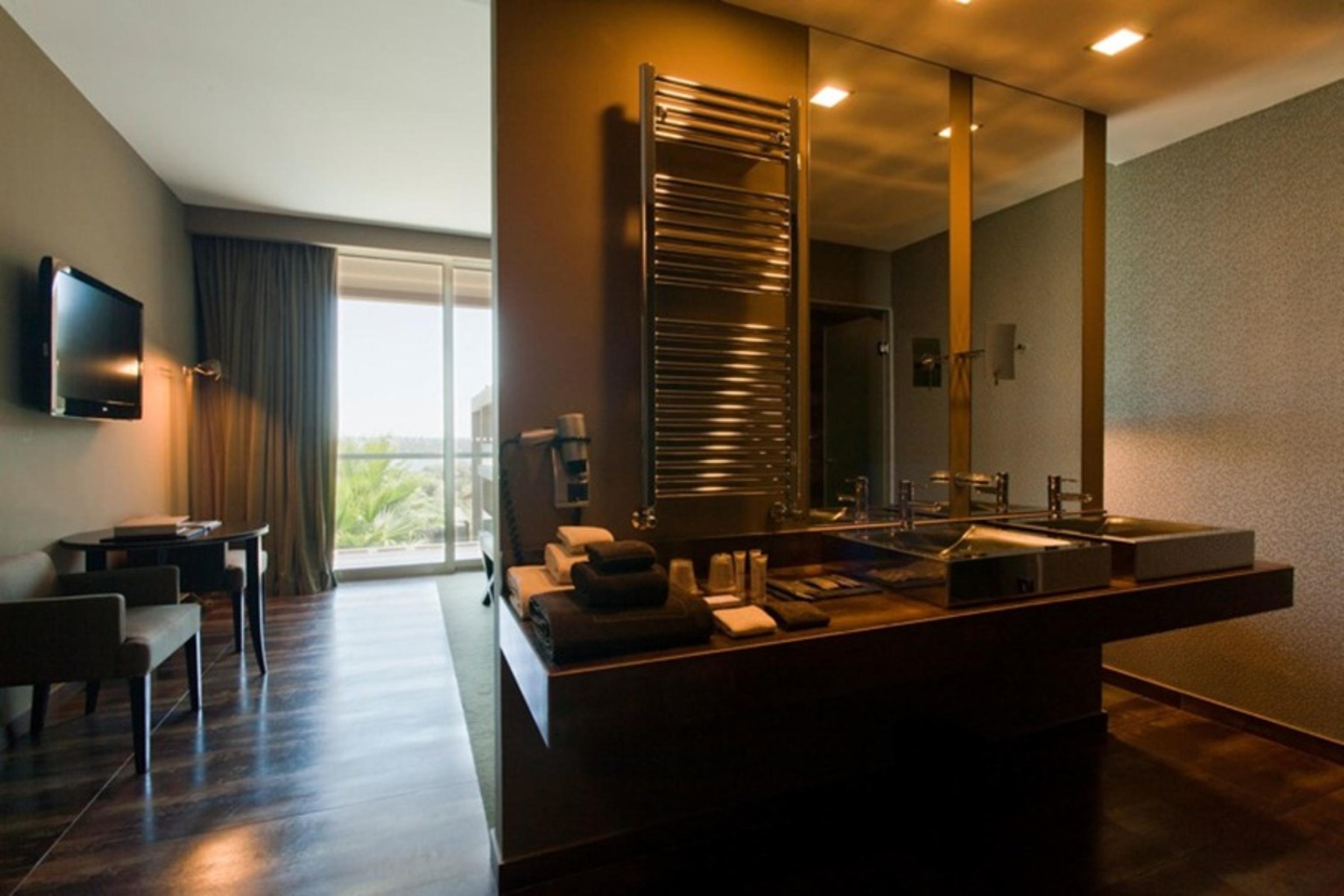 Lago Montargil&Villas Esterno foto The photo displays a modern hotel room with a contemporary design. The room features a large window, allowing natural light to enter and offering a view outside. On one side, there is a sitting area with a small table and chairs. The other side showc