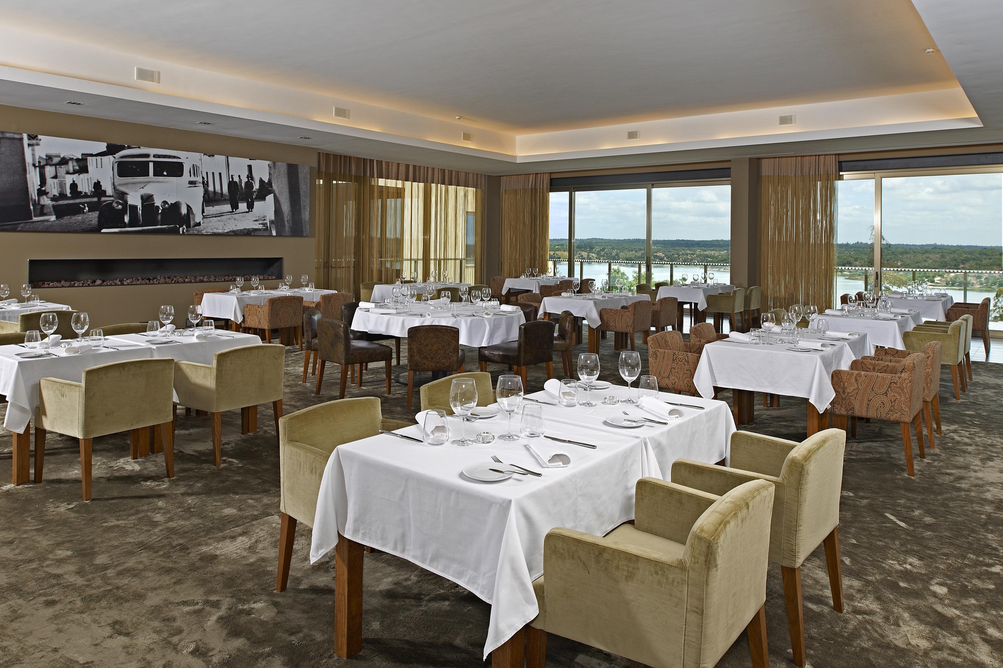 Lago Montargil&Villas Esterno foto The photo shows an elegant restaurant interior featuring neatly arranged tables with white tablecloths. Each table is set with plates, cutlery, and glasses. The seating includes a mix of upholstered chairs in different colors—some light and others da