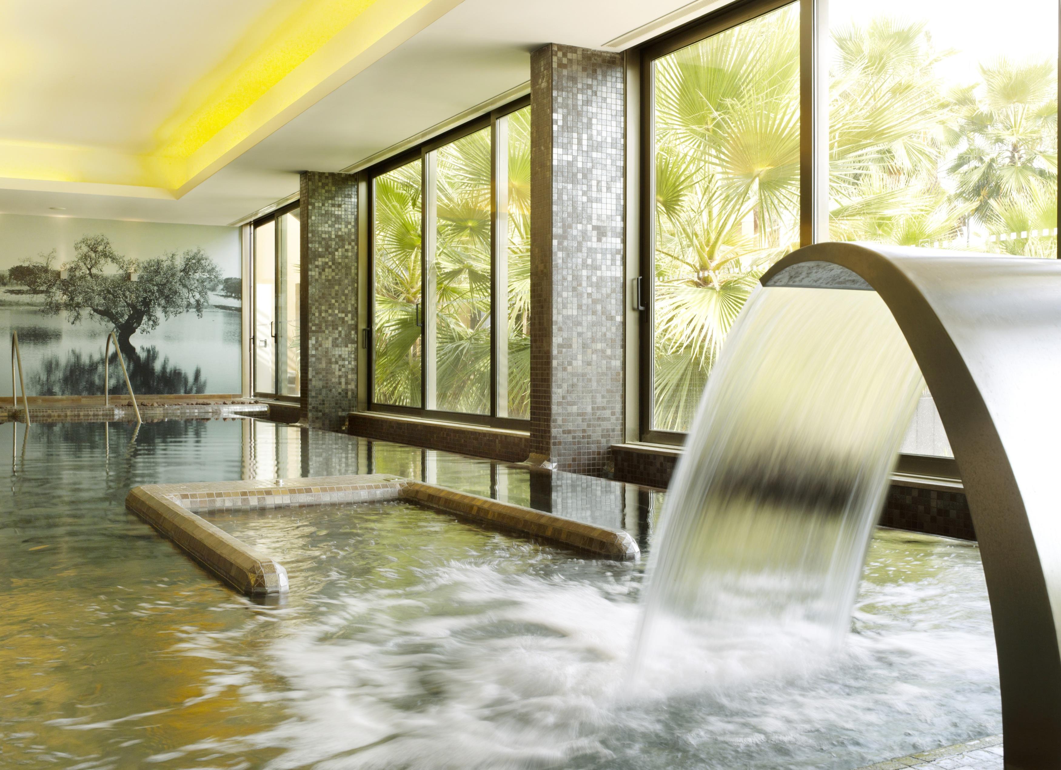 Lago Montargil&Villas Esterno foto The photo depicts a serene spa environment featuring a tranquil indoor pool area. There is a sleek, modern water feature that spills water gracefully into the pool. Large windows allow natural light to flood the space, showcasing views of lush greene