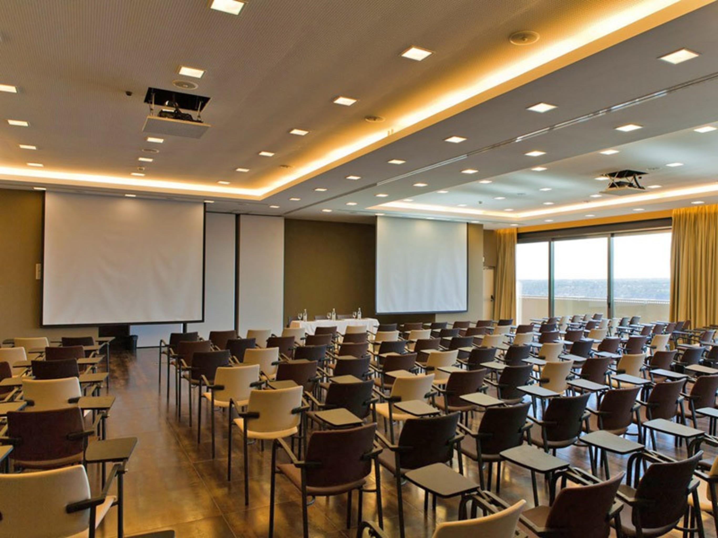 Lago Montargil&Villas Esterno foto The photo shows a large conference room set up for a presentation or meeting. There are multiple rows of chairs arranged in a semi-theater style, facing two large projection screens. The room has a modern design, with soft lighting and large windows 
